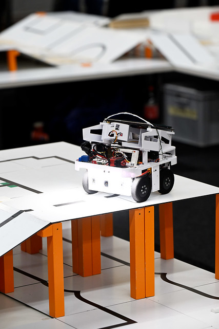 A small robot on a raised white RoboCupJunior Rescue Line course, following a black line across orange supports.
